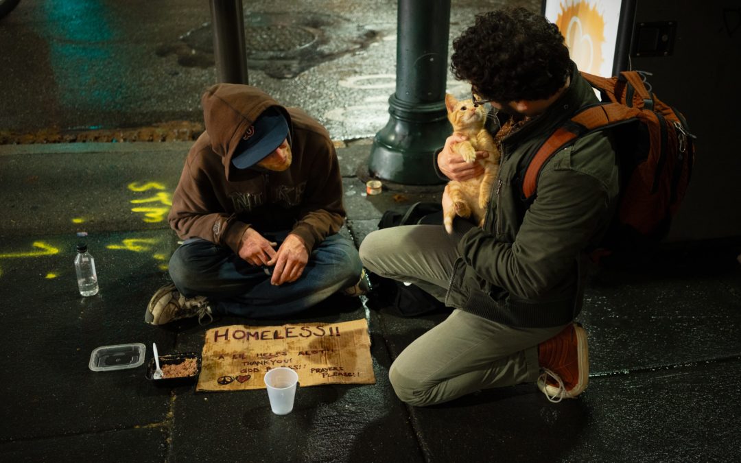 man sleeping on street with a man holding a cat