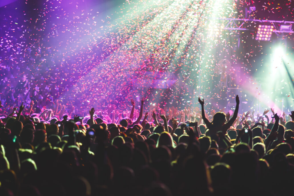 A crowded concert hall with scene stage lights, rock show performance, with people silhouettes during live music show performance with crowd of audience