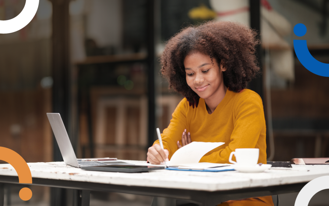 A woman sitting at a desk with her laptop open. She's smiling while working.