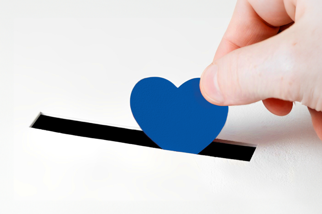 A blue heart being put into a donation box.