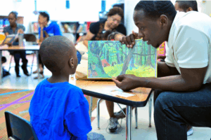 A man reads a book to a child in a setting that looks like a public library.