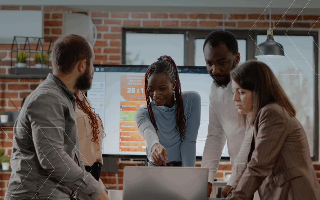 A diverse group of people huddle around a laptop. They look focused and hard at work.